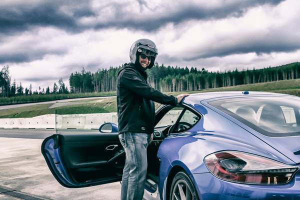 Man standing, smiling near a blue Porsche at the Vancouver Island Motorsport Circuit